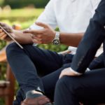 a person on a tablet talking to someone while sitting on a park bench