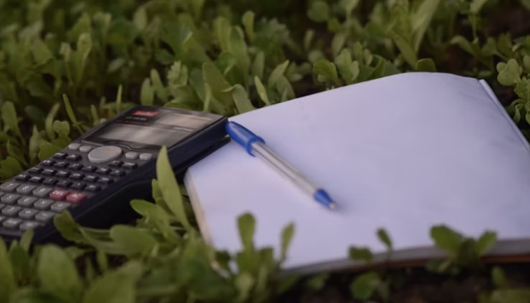 a calculator and a piece of paper with a pen on it lying together in a grass field