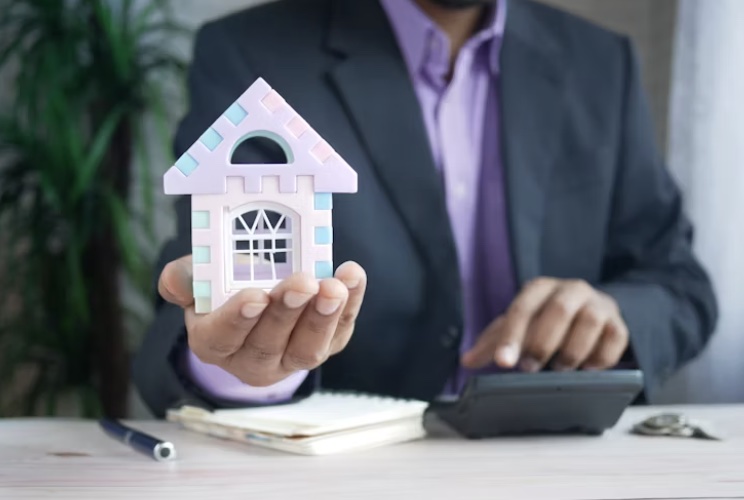 a person holding up a hand sized image of a house to signify the sale of a house