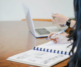 a person sitting a table with another person on a computer