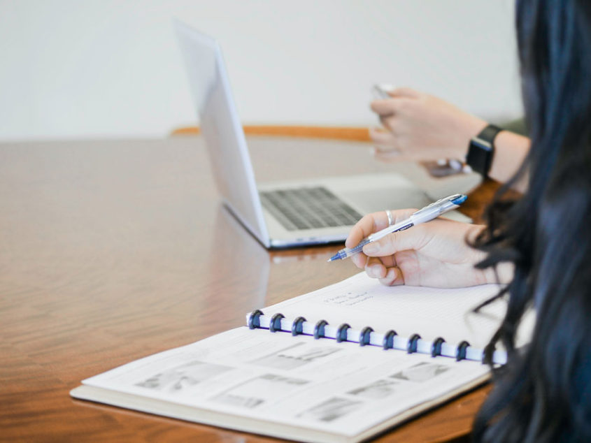 a person sitting a table with another person on a computer